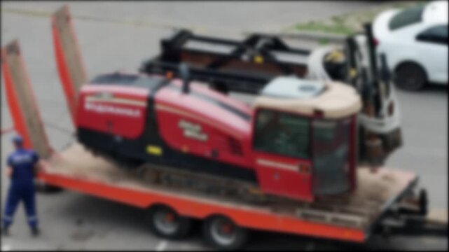 A lowboy trailer is being used to transport a modern horizontal boring machine for laying water pipes and electrical cables underground, renovation work, blurry
