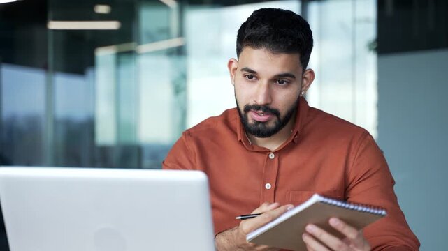 Confident businessman watching video call conference or training notes in notebook looking at laptop screen sitting at workplace in business office. The manager communicates remotely online. Close up