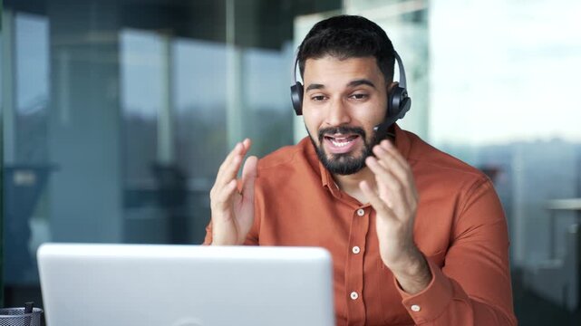 Confident businessman in a headset talking on a video call using laptop sitting at workplace in office. Entrepreneur has a business meeting. Manager speaks remotely at an online conference. Close up