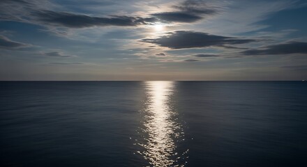 Obraz premium Moonlight reflecting on the ocean surface under a cloudy sky creating a serene and peaceful scene