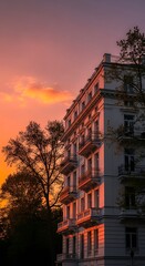 Building facade with balconies at sunset with orange and pink sky and silhouette of trees around it