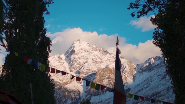 Slow motion shot of defocused prayer flags waving in front of snowy Himalayan mountain peak during the sunset as seen from Keylong in Lahaul and Spiti district, Himachal Pradesh, India. Scenic view. 