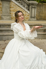 Obraz premium figure of female blonde model wearing white fantasy wedding gown. romantic sitting pose on staircase of historical fairytale castle location 