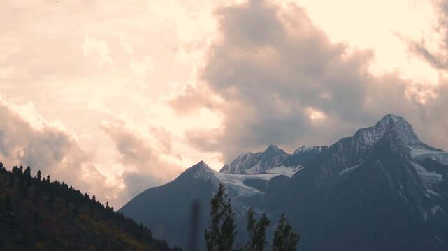 Landscape shot of orange clouds above the snowy Himalayan mountain peak during the sunset as seen from Keylong in Lahaul and Spiti district, Himachal Pradesh, India. Scenic view of sunset in autumn.