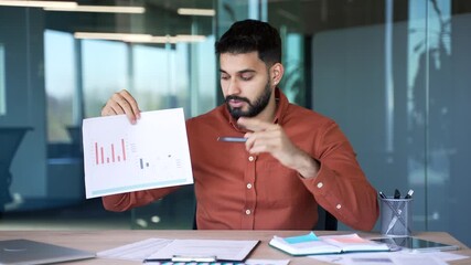 Webcam view. Professional male manager presenting chart data by video call looking at camera at workplace in office. Businessman discussing growth statistics. Business meeting, analysis, and teamwork - Powered by Adobe