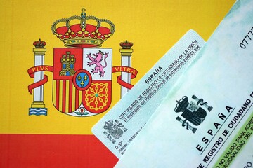 Citizenship or naturalization certificate document and card on flag of Spain close up