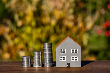 Small toy gray house model and stack of coins on wooden table, outdoors, closeup. Concept of planning to save money for the purchase or construction of a home, mortgage and real estate investment