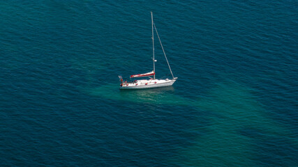 Fototapeta premium Aerial view of a white sailboat sailing in the blue and calm sea.