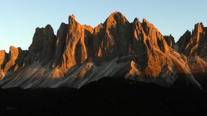 Cinematic aerial view of Dolomites Italy at sunrise, rugged rocky peaks above lush alpine hills and scattered chalets, serene mountain travel landscape nature scenery - Powered by Adobe