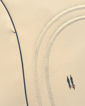 Aerial view of two figures walking, casting long shadows on the pale sand crossed by tire tracks, Vil nohirs k, Dnipropetrovsk Oblast, Ukraine.