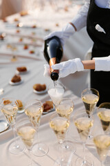 The waiter pours champagne into glasses before the celebration