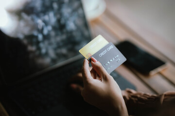 A woman holds a credit card and a smartphone, often shopping or conducting financial transactions online.