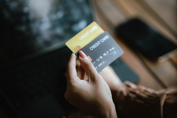 A woman holds a credit card and a smartphone, often shopping or conducting financial transactions online.