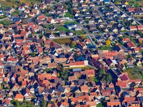 Aerial view of tightly packed houses with warm terracotta roofs contrast with the green trees and blue sky, Rouffach, Grand Est, France.