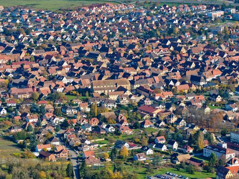 Aerial view of terracotta roofs blanketing the landscape, punctuated by the towering spire of the church, creating a tapestry of human habitation, Rouffach, Grand Est, France.