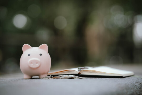 A pink piggy bank with scattered coins and an open notebook placed on a stone surface, symbolizing financial planning, saving money, and personal budgeting. - Powered by Adobe