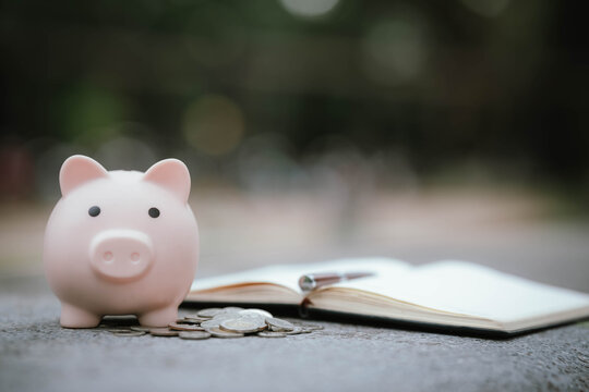 A pink piggy bank with scattered coins and an open notebook placed on a stone surface, symbolizing financial planning, saving money, and personal budgeting.