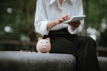 A person saves money by putting coins into a pink piggy bank while holding a calculator, symbolizing financial planning, saving, and budgeting.