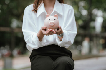 A person saves money by putting coins into a pink piggy bank while holding a calculator, symbolizing financial planning, saving, and budgeting.