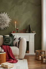 Living room decorated for Christmas with a beige sofa, green wall, and red accents. Cozy and stylish holiday atmosphere.