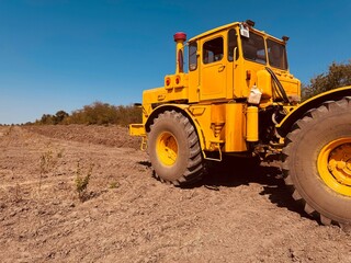 A beautiful old yellow tractor after work in the field against the blue sky.