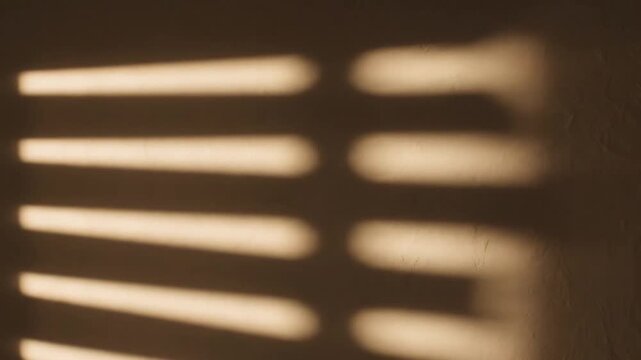 Warm golden sunbeams filter through parallel slats, casting distinct, blurred stripes of light and shadow onto a textured brown wall, evoking a tranquil, cozy morning or afternoon scene.