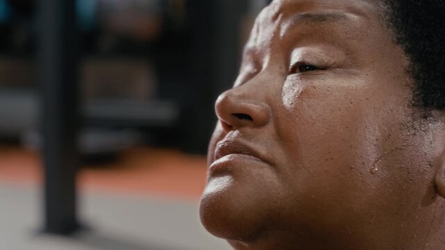 Close up shot of exhausted mature Black woman wiping sweat off her forehead after intense workout in gym and then smiling being proud of herself and leading active lifestyle