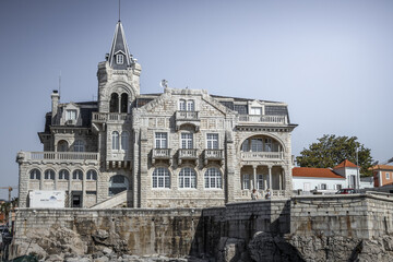 View of a grand, ornate building standing proudly above the rocky coastline, its intricate stonework and architectural details bathed in the soft daylight, Cascais, Lisbon, Portugal.