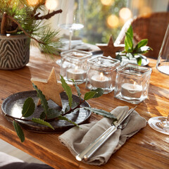 Atmospheric christmas table decoration in a cozy conservatory with festive bokeh lights. Romantic christmas dinner concept with lit candles in a restaurant. Gastronomy background.