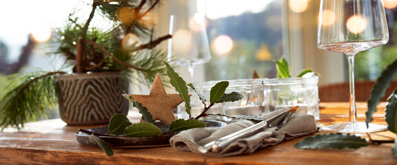 Atmospheric christmas table decoration in a cozy conservatory with festive bokeh lights. Romantic christmas dinner concept with lit candles in a restaurant. Horizontal gastronomy background.