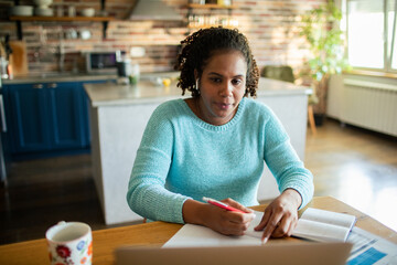 Adult woman concentrating while studying with laptop at home kitchen