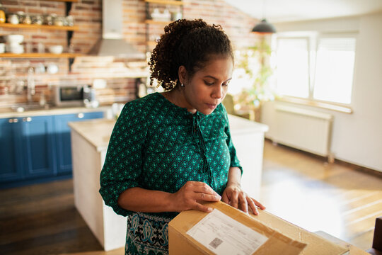Adult woman focused opening delivery box in home kitchen