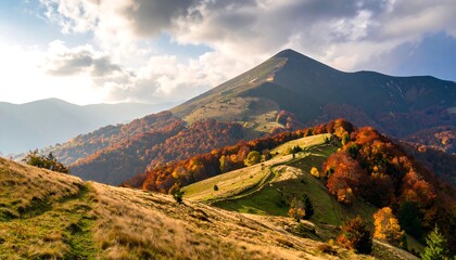 Scenic mountain landscape showcases autumn foliage and a winding trail on a sunlit ridge. Colorful trees adorn the hillsides with clouds overhead