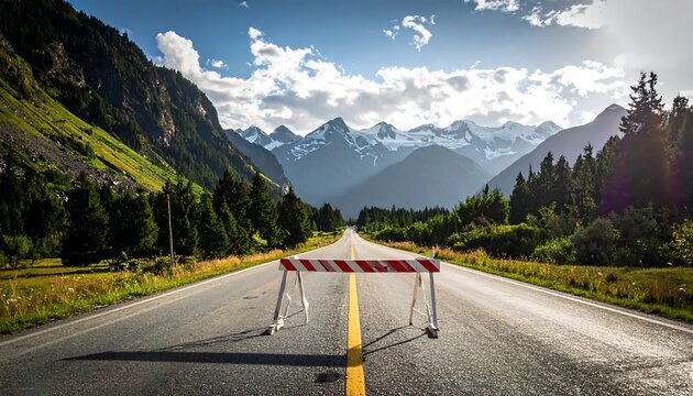 Scenic shot of an empty highway obstructed by a barricade. The road stretches into a mountain range under a partly cloudy sky. Lush trees line the route