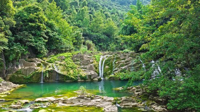 Beautiful waterfall cascading over mossy rocks into a tranquil emerald pool in lush green jungle, Guizhou.