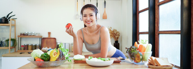 Happy asian fitness woman listening to music with headphones and preparing a vegetable salad in the...