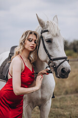 Fototapeta premium Young caucasian female in red dress with white horse in outdoor setting