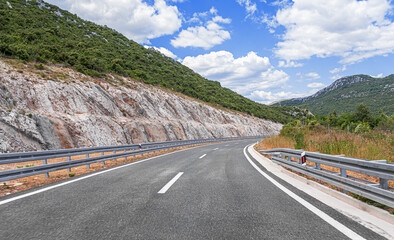 A winding highway runs through a scenic mountain landscape under a bright blue sky with clouds, offering a peaceful route for travel and adventure.