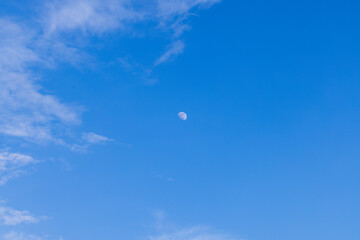 Daytime sky and clouds with moon,Half moon visible in blue sky during daytime,A square photograph showing a bright daytime moon surrounded by soft clouds.