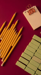 Fototapeta premium Top view of yellow pencils, erasers, and notebook on a burgundy surface, representing education, learning and office supplies for creative work