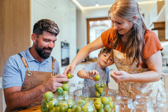 Parents and little son canning greengage plums together at home kitchen table