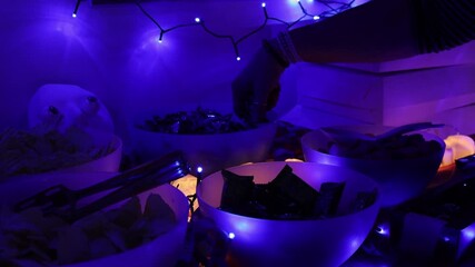 Hands serving Halloween-themed snacks and spooky treats onto a plate during a festive Halloween party. Decorative pumpkins, candles, and creepy elements create a dark atmospheric holiday mood, capture