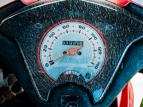 The motorcycle speedometer appears cracked from heat exposure, showing worn plastic texture and highlighting aging vehicle parts in daily use.