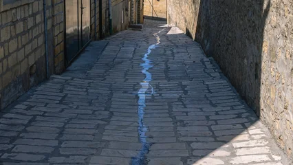 Fototapete Rund Enge Straßen The water flows through the ancient narrow streets of the ancient city. Ancient quarters of the city of Derbent. Ancient sandstone houses. Narrow streets in an ancient city in the Caucasus.  © Eduard Belkin