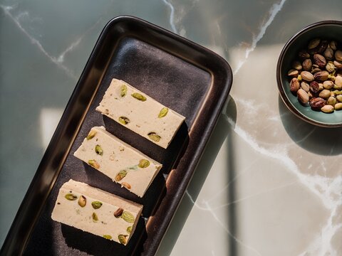 Sweet nougat bars with pistachios on a dark tray with a bowl of nuts