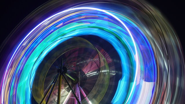 close-up of a spinning ferris wheel, where the long exposure photography technique renders the lights as intense