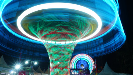 A dynamic night image of an amusement ride, captured using a long exposure technique to transform the bright neon lights into sweeping, circular blue and green light trails