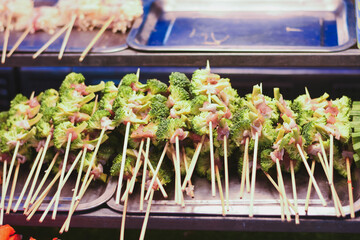 Broccoli and meat skewers arranged on metal trays for grilling.