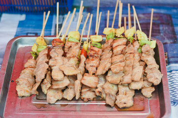 Grilled pork skewers on a tray, some with vegetables.