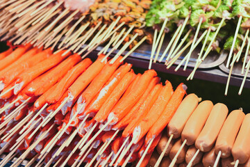 Many bright orange crab sticks on skewers at a food stall.